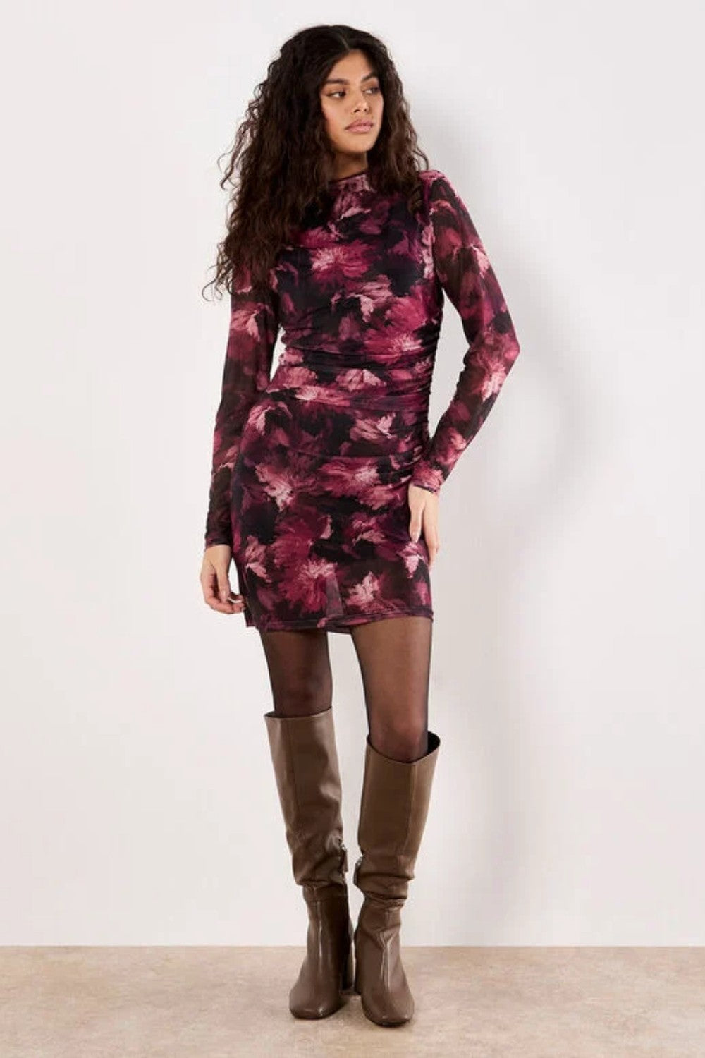 Woman wearing a long-sleeve, patterned dress against a white background