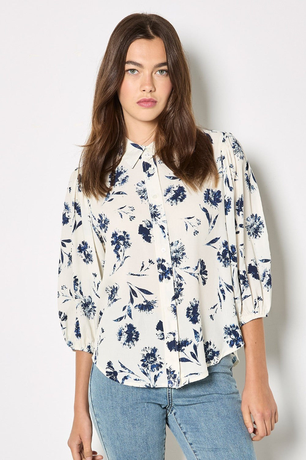 Woman wearing a white blouse with blue floral pattern and blue jeans on a white background
