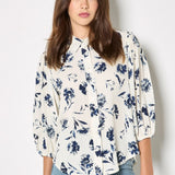 Woman wearing a white blouse with blue floral pattern and blue jeans on a white background