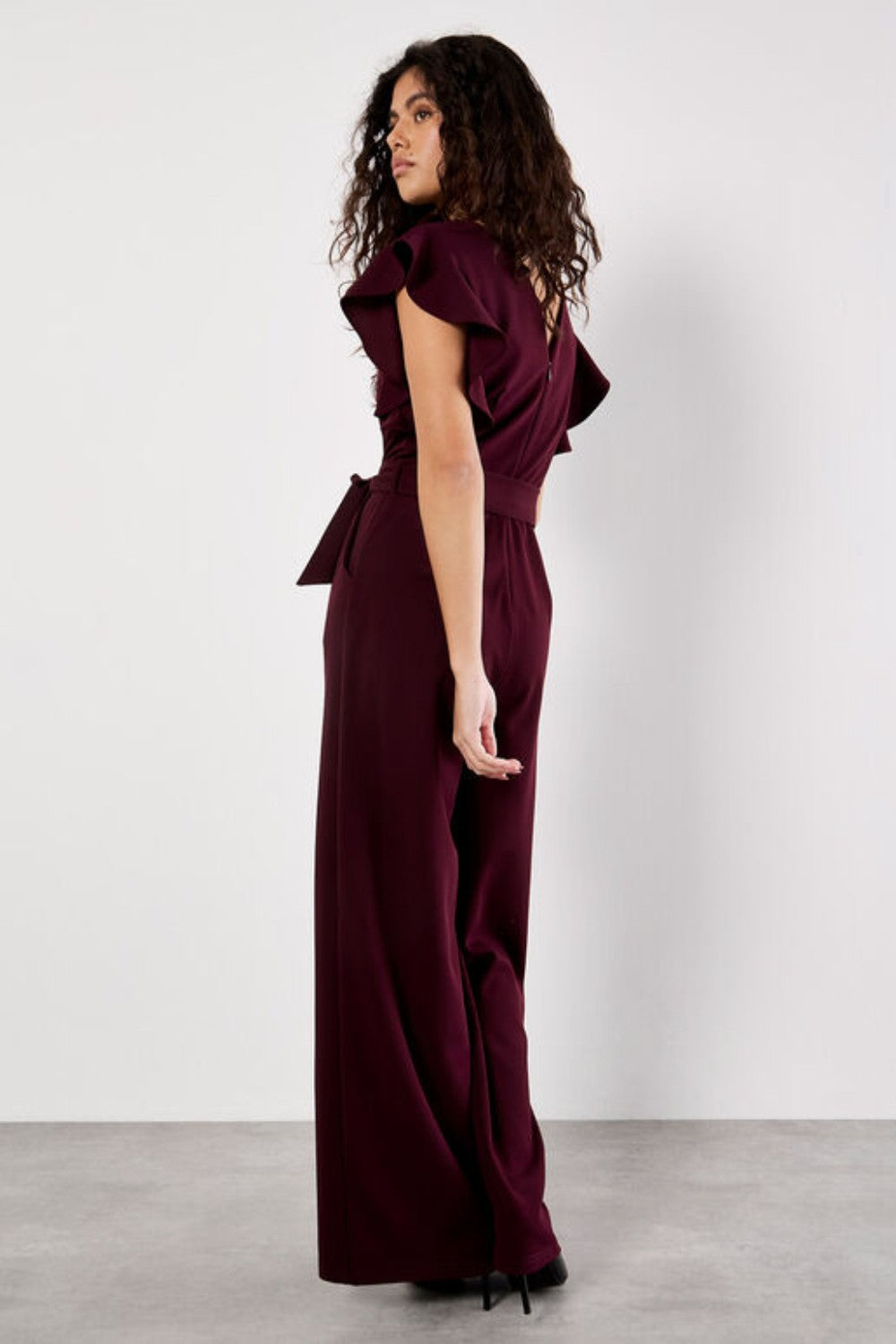 Woman wearing a burgundy jumpsuit with ruffled sleeves against a white background