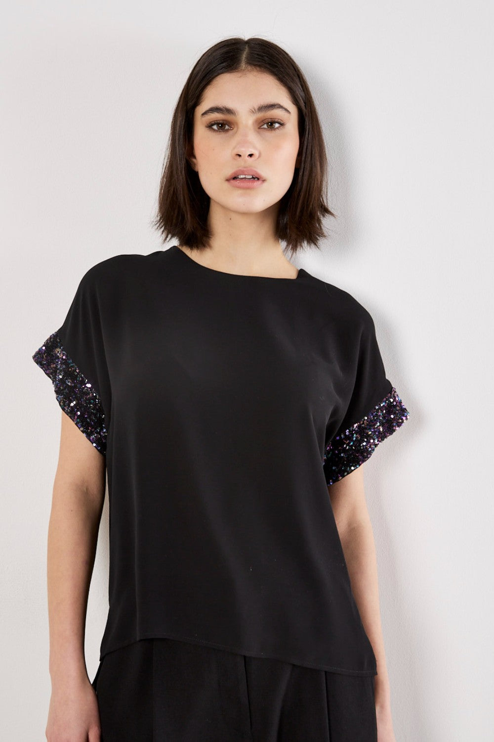 Woman wearing a black top with sequin sleeves on a white background