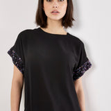 Woman wearing a black top with sequin sleeves on a white background