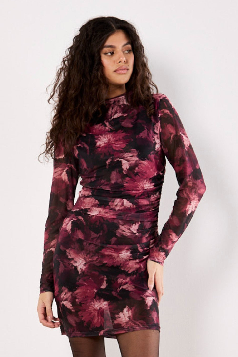Woman wearing a long-sleeve, patterned dress against a white background