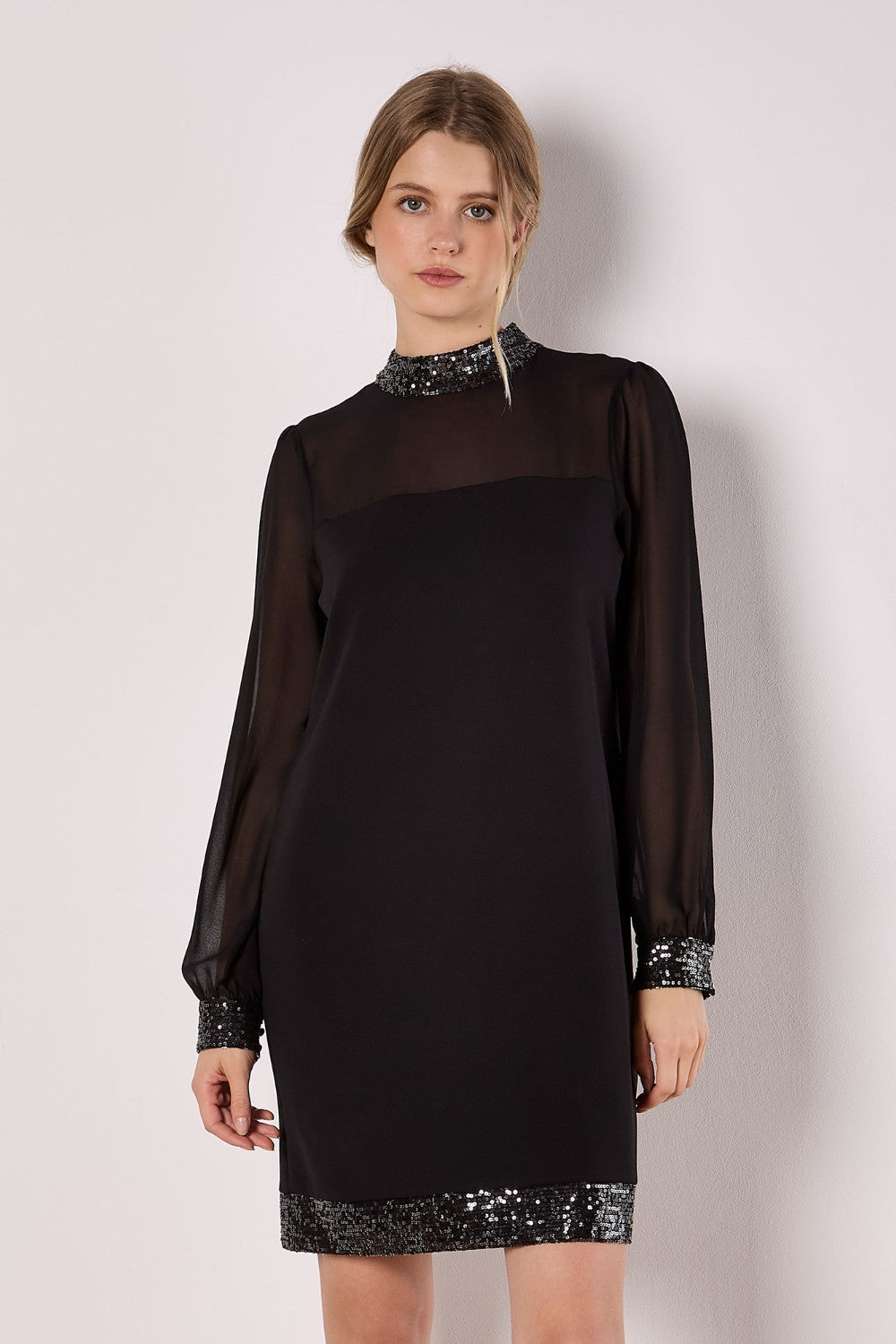 Woman wearing a black dress with sequin details on a plain background