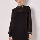 Woman wearing a black dress with sequin details on a plain background