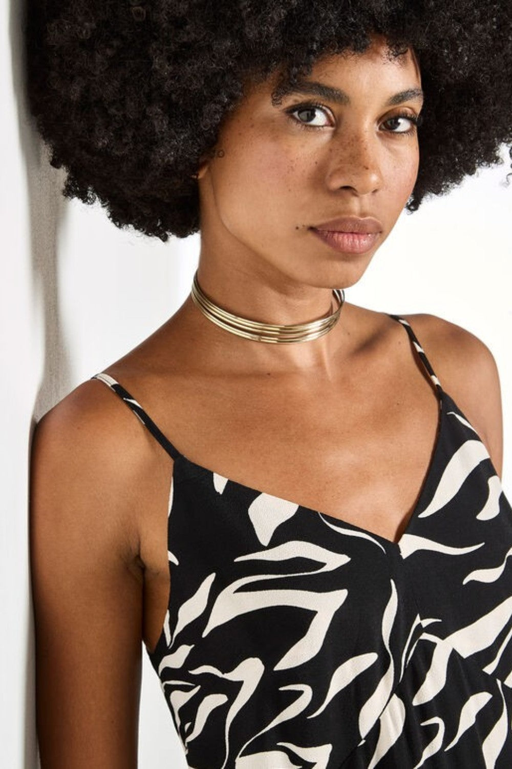 Woman wearing a black and white patterned top with a gold necklace against a white background