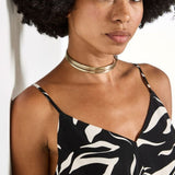 Woman wearing a black and white patterned top with a gold necklace against a white background