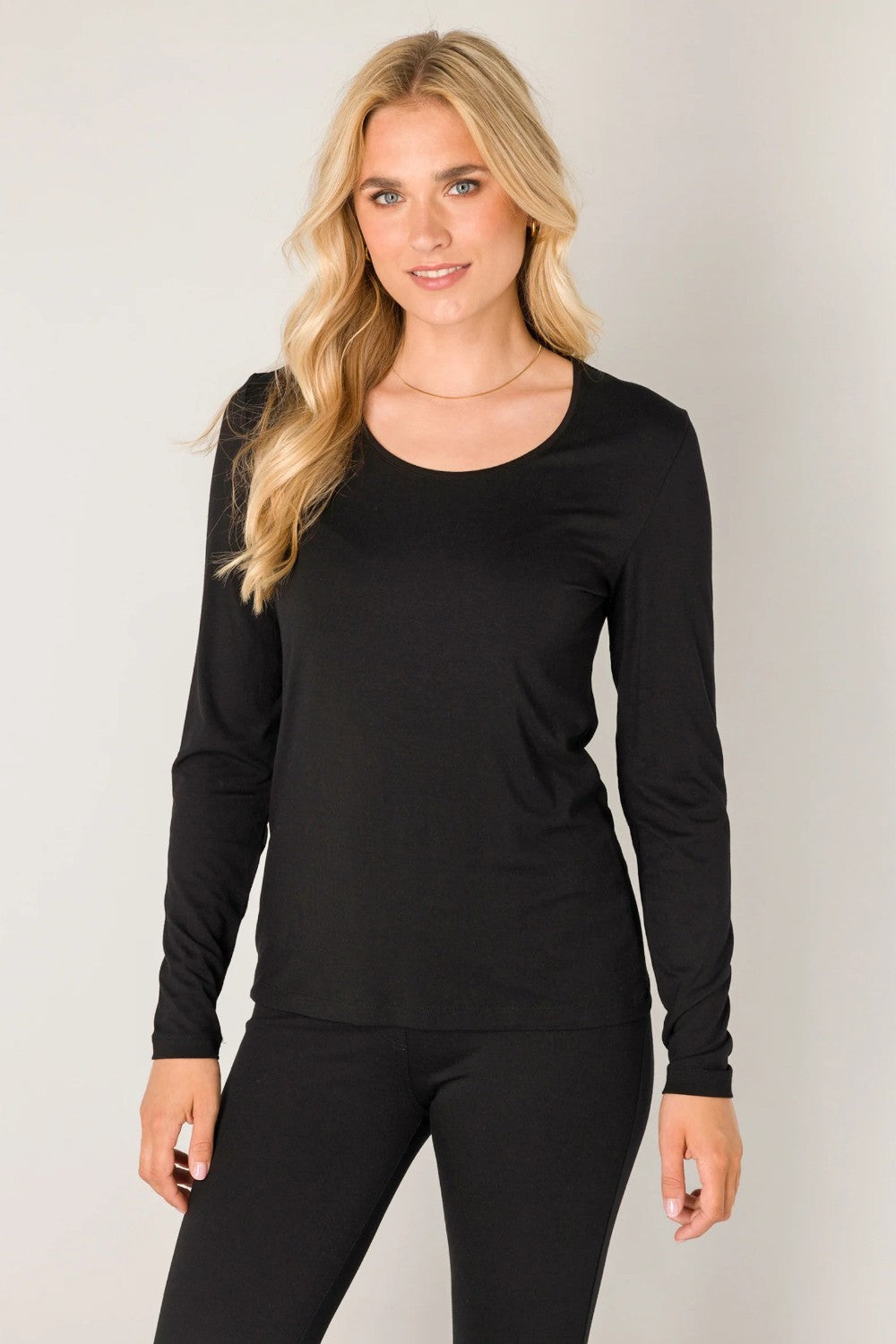 Woman wearing a black long-sleeve top and black pants against a plain background