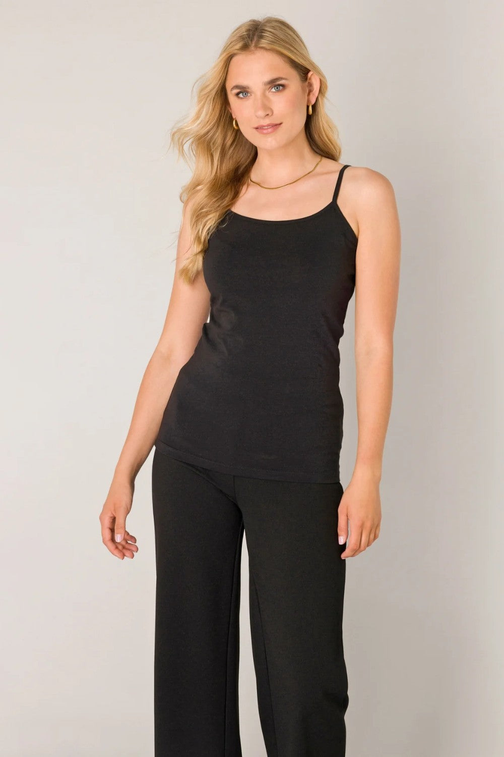 Woman wearing a black camisole with black pants on a light background.