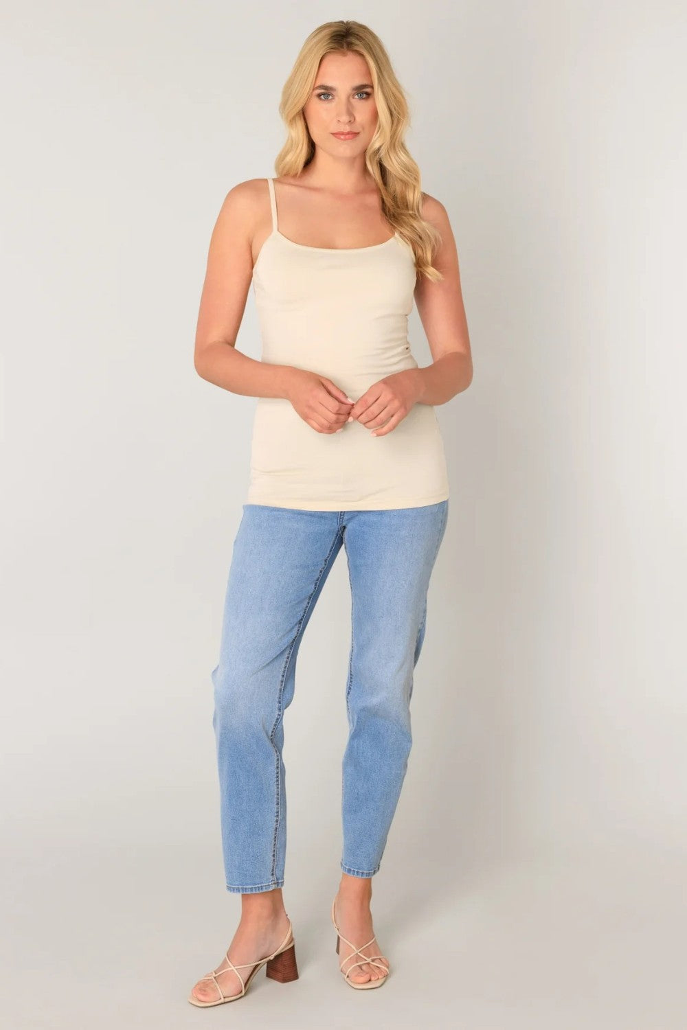 Woman wearing a beige tank top and light blue jeans on a plain background