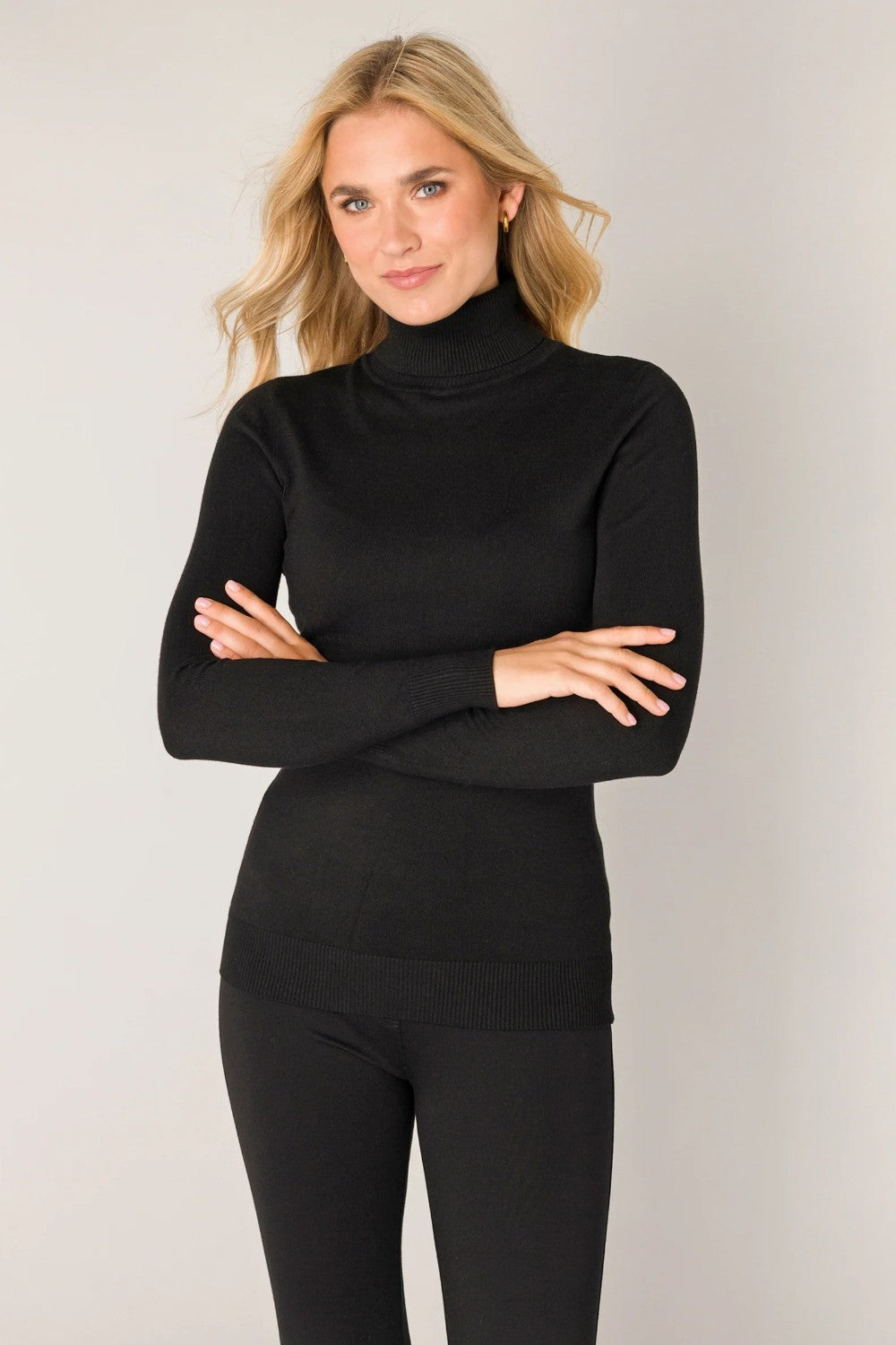 Woman wearing a black turtleneck and pants against a plain background