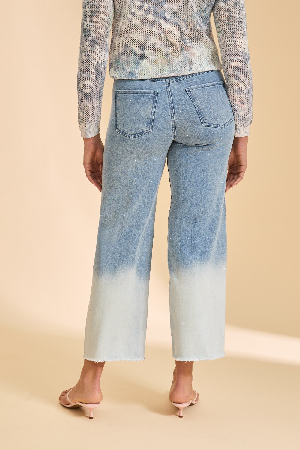 Person wearing a patterned top and light blue jeans with a gradient effect on a beige background