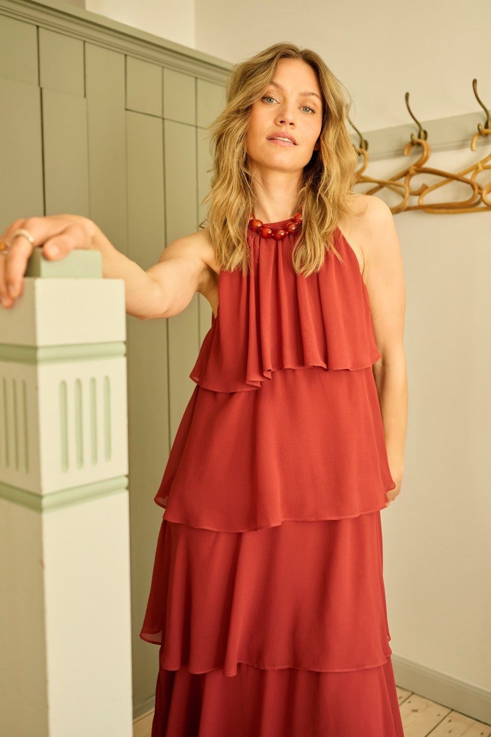 Woman wearing a red dress standing in a room with wooden flooring and a white wall.