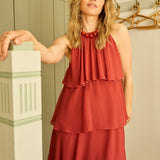 Woman wearing a red dress standing in a room with wooden flooring and a white wall.