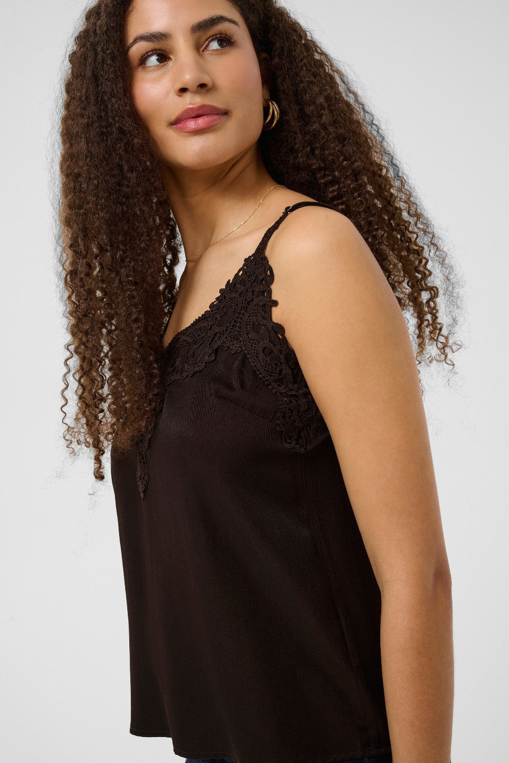 Woman wearing a brown lace-trimmed top against a white background