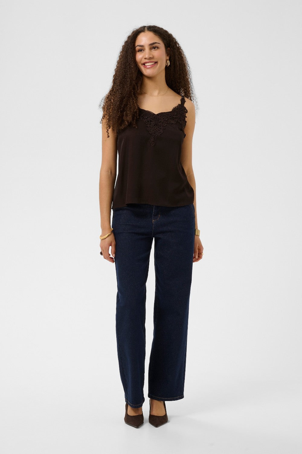 Woman wearing a brown top and dark blue jeans on a white background