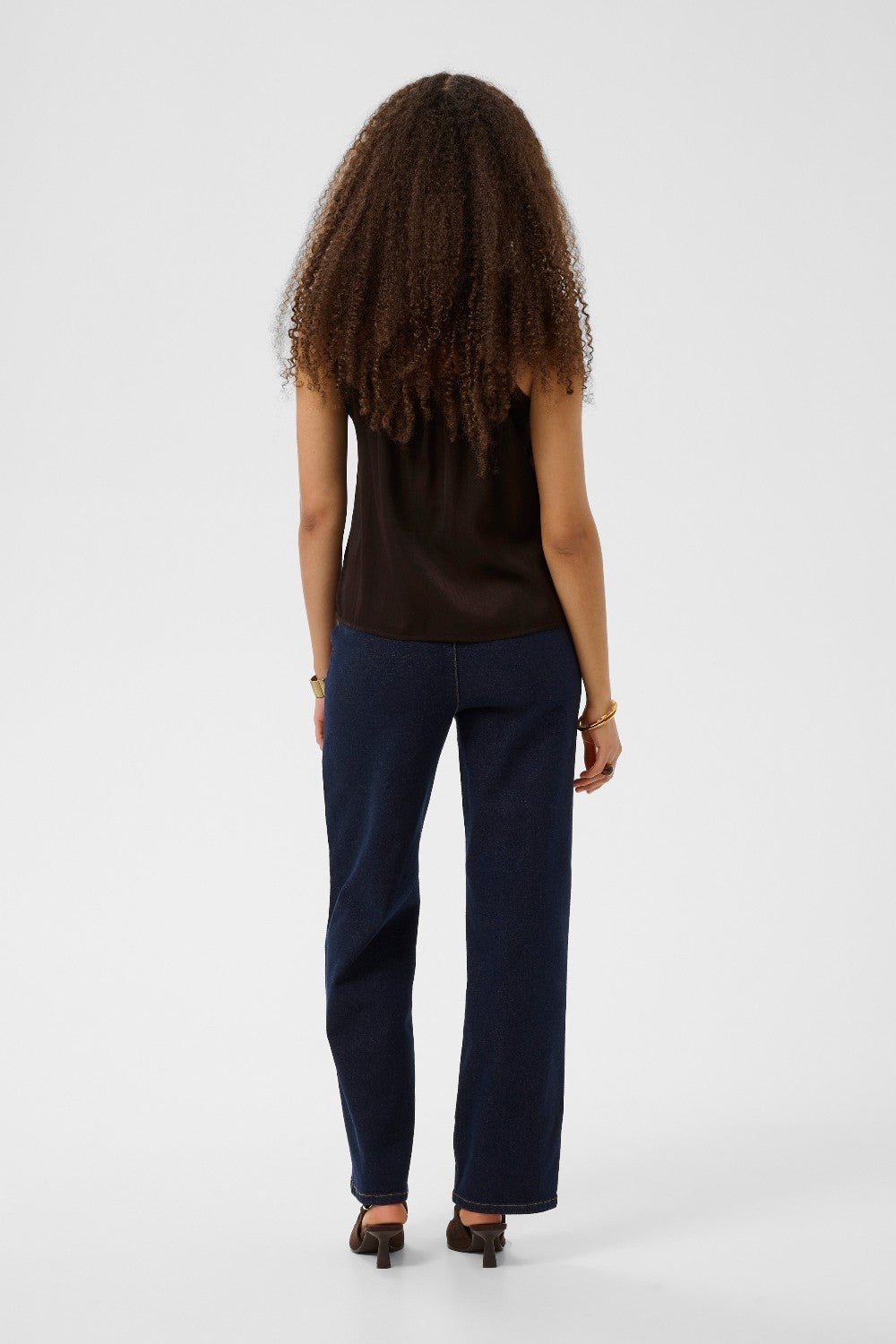 Person wearing a brown sleeveless top and blue pants on a white background