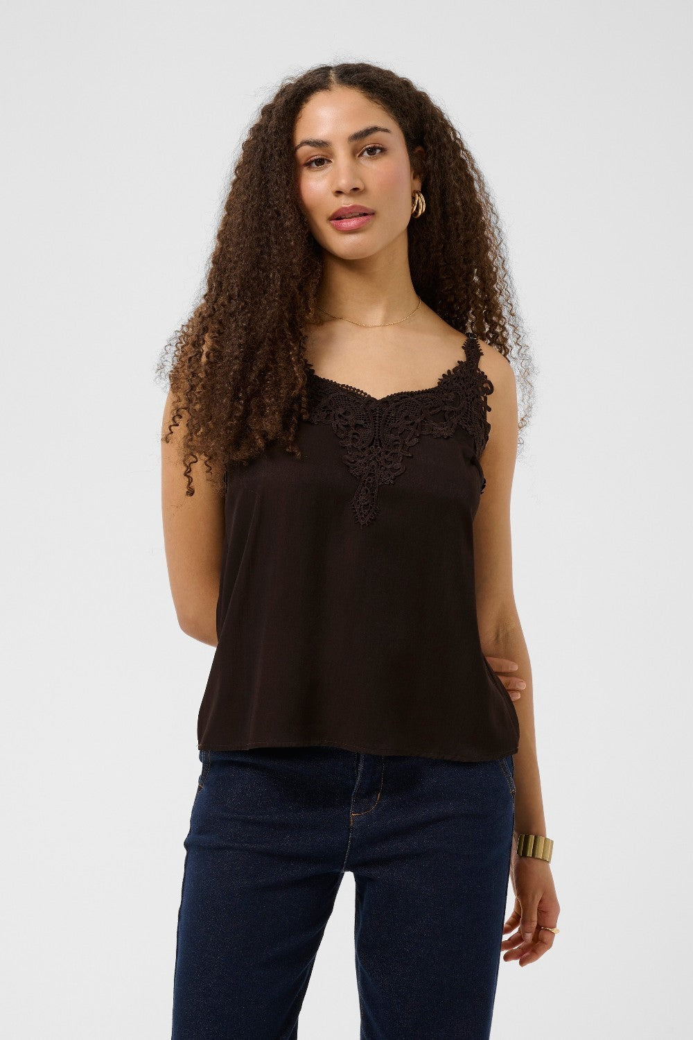 Woman wearing a brown sleeveless top with lace details and blue jeans on a white background