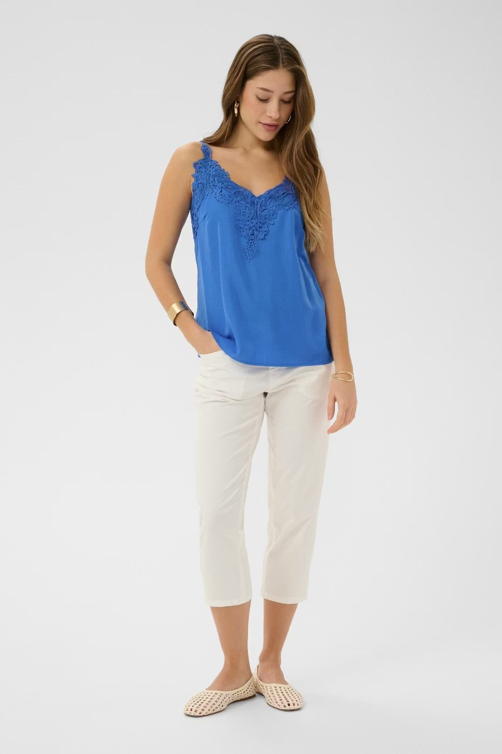 Woman wearing a blue sleeveless top and white pants on a light gray background