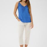 Woman wearing a blue sleeveless top and white pants on a light gray background