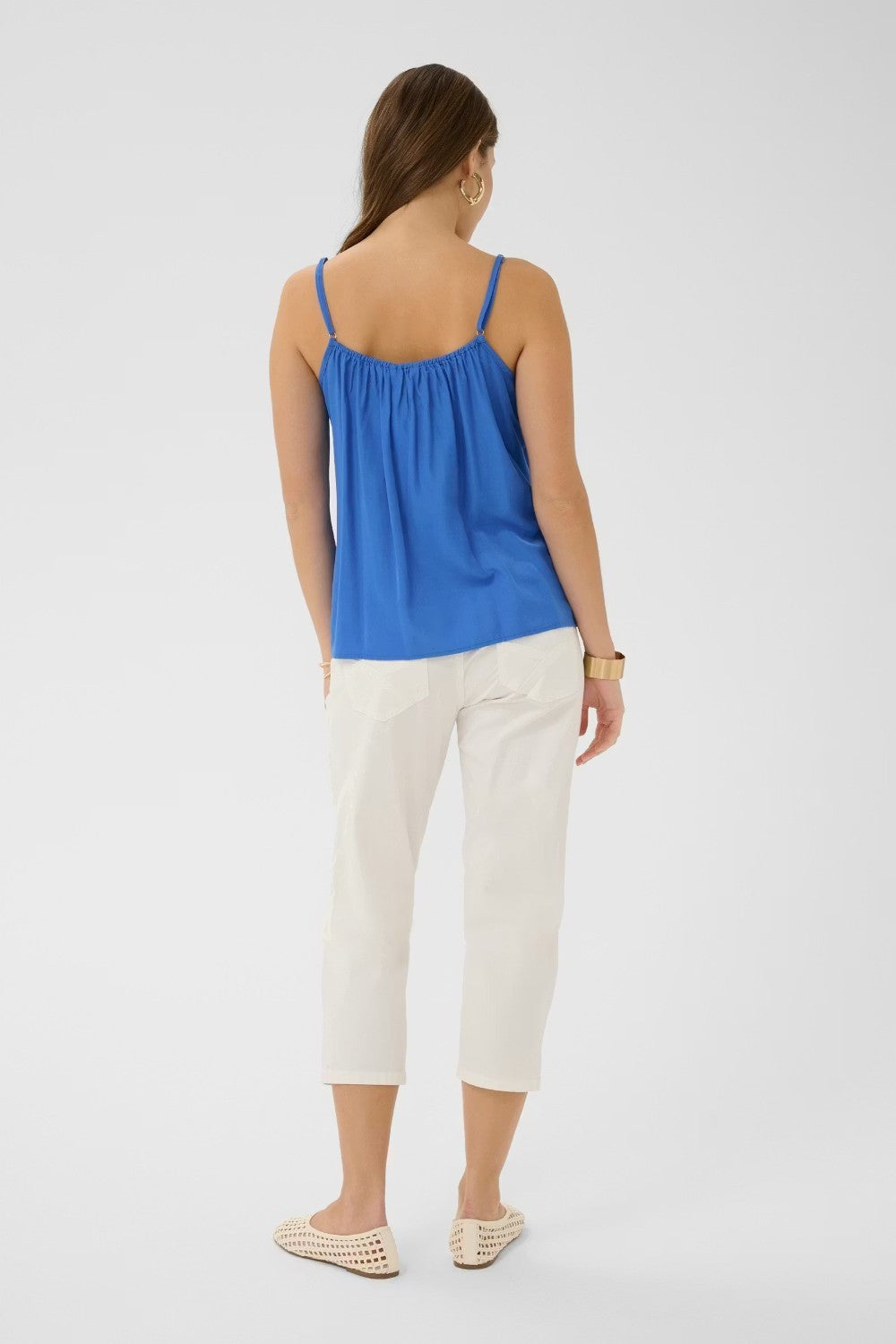 Woman wearing a blue top and white pants on a light gray background