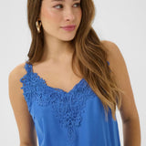 Woman wearing a blue sleeveless top with lace detailing on a white background