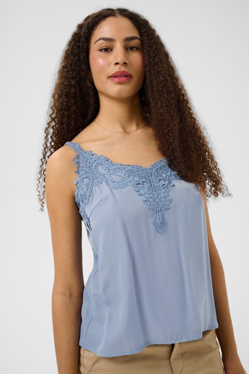 Woman wearing a light blue sleeveless top with lace details on a white background
