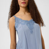 Woman wearing a light blue sleeveless top with lace details on a white background