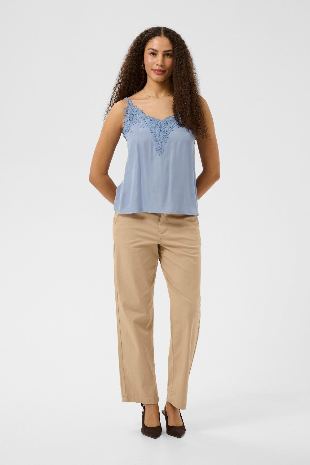 Woman wearing a light blue sleeveless top with lace details on a white background