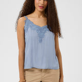 Woman wearing a light blue sleeveless top with lace details on a white background