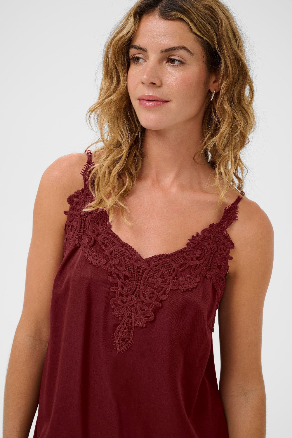 Woman wearing a burgundy sleeveless top with lace detailing on a white background