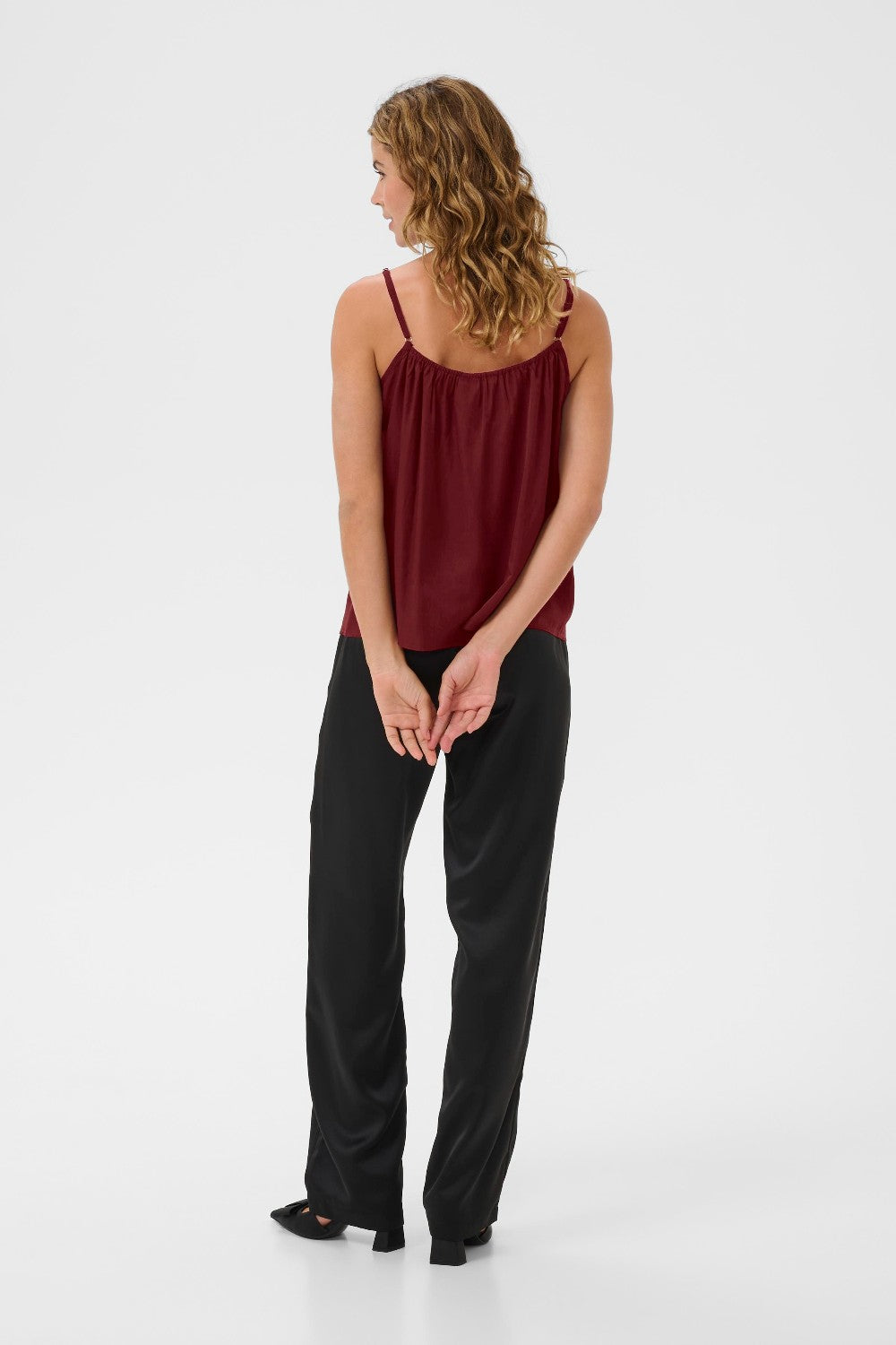 Woman wearing a burgundy top and black pants on a white background