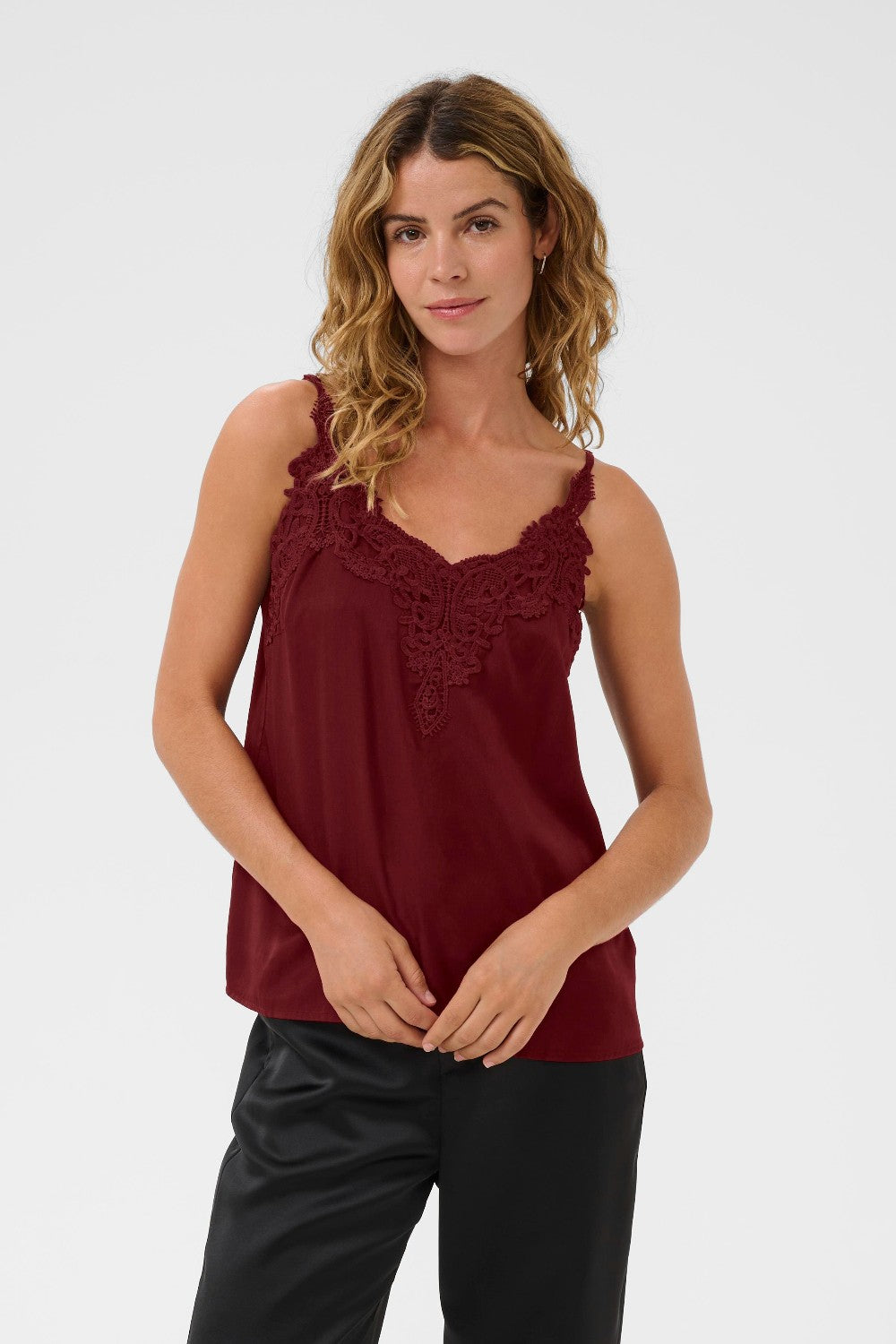Woman wearing a burgundy sleeveless top with lace details on a white background