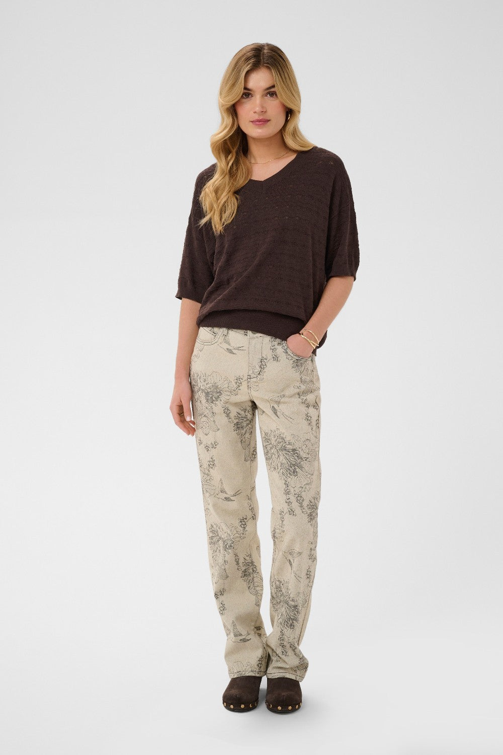 Woman wearing a brown top and patterned beige pants on a white background
