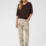 Woman wearing a brown top and patterned beige pants on a white background