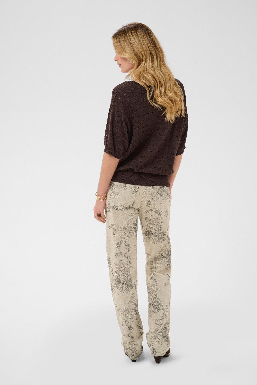 Woman wearing a brown top and patterned beige pants on a white background