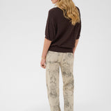 Woman wearing a brown top and patterned beige pants on a white background