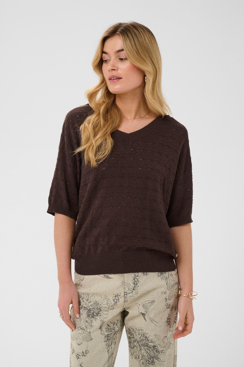 Woman wearing a brown sweater and patterned pants on a white background