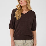 Woman wearing a brown sweater and patterned pants on a white background