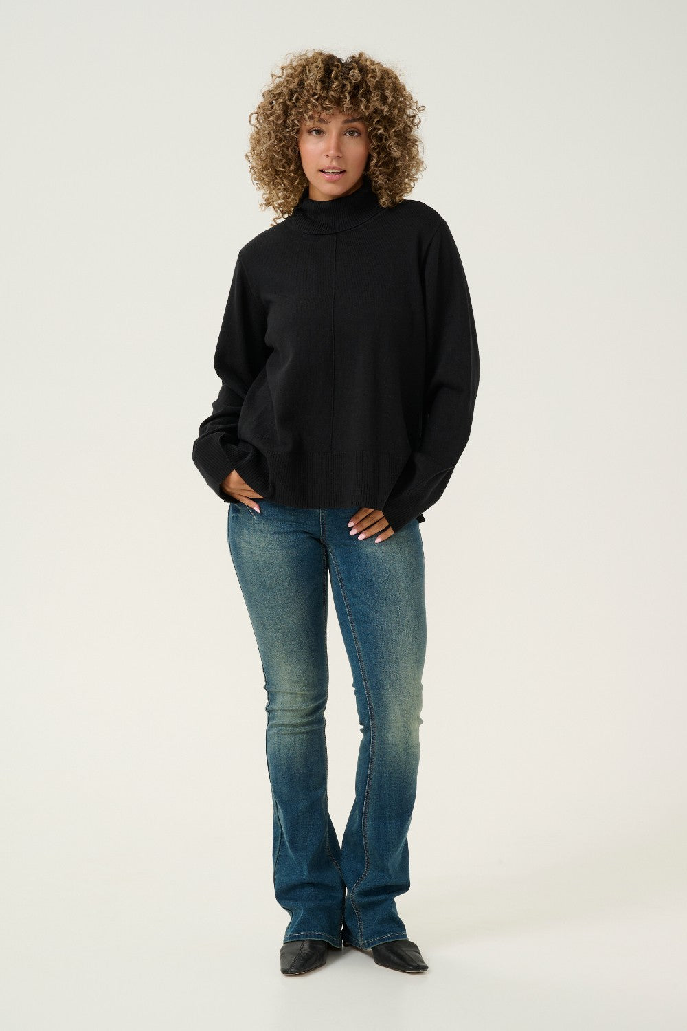 Person wearing a black turtleneck and blue jeans on a white background