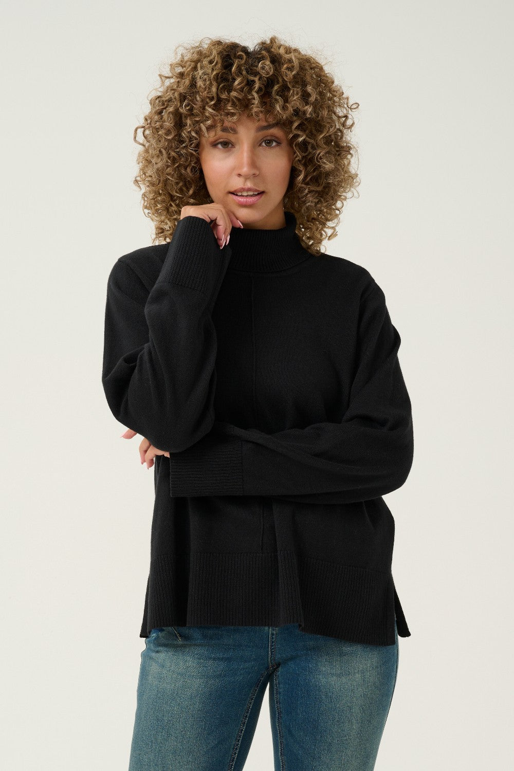 Woman wearing a black turtleneck sweater and blue jeans against a white background