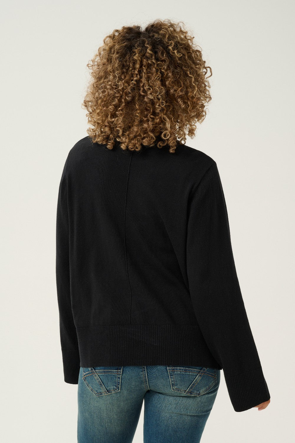 Person wearing a black long-sleeve top and blue jeans on a plain background