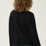 Person wearing a black long-sleeve top and blue jeans on a plain background
