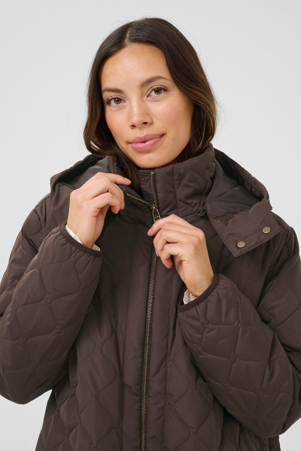 Woman wearing a brown quilted jacket against a plain background