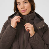 Woman wearing a brown quilted jacket against a plain background