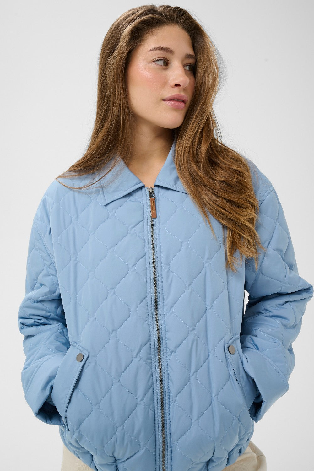 Woman wearing a light blue quilted jacket against a white background