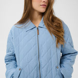 Woman wearing a light blue quilted jacket against a white background