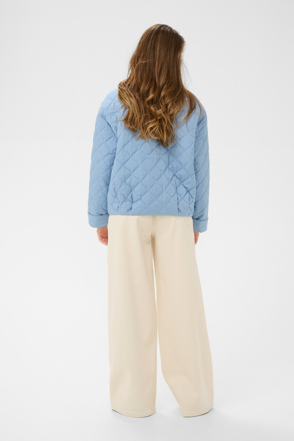Person wearing a blue quilted jacket and beige pants on a white background