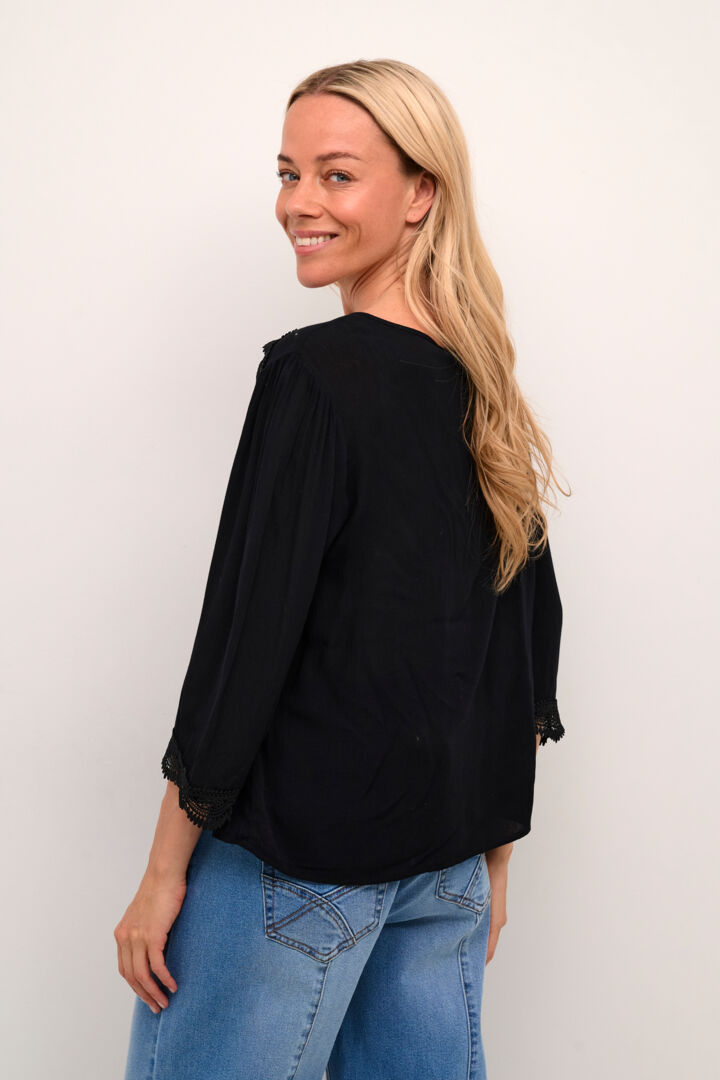 The Cream Bea 3/4 Sleeve Lace Blouse features a sleek black colour and a charming front tie with tassels. Elevate any outfit with this versatile piece, perfect for adding a touch of sophistication to your wardrobe.