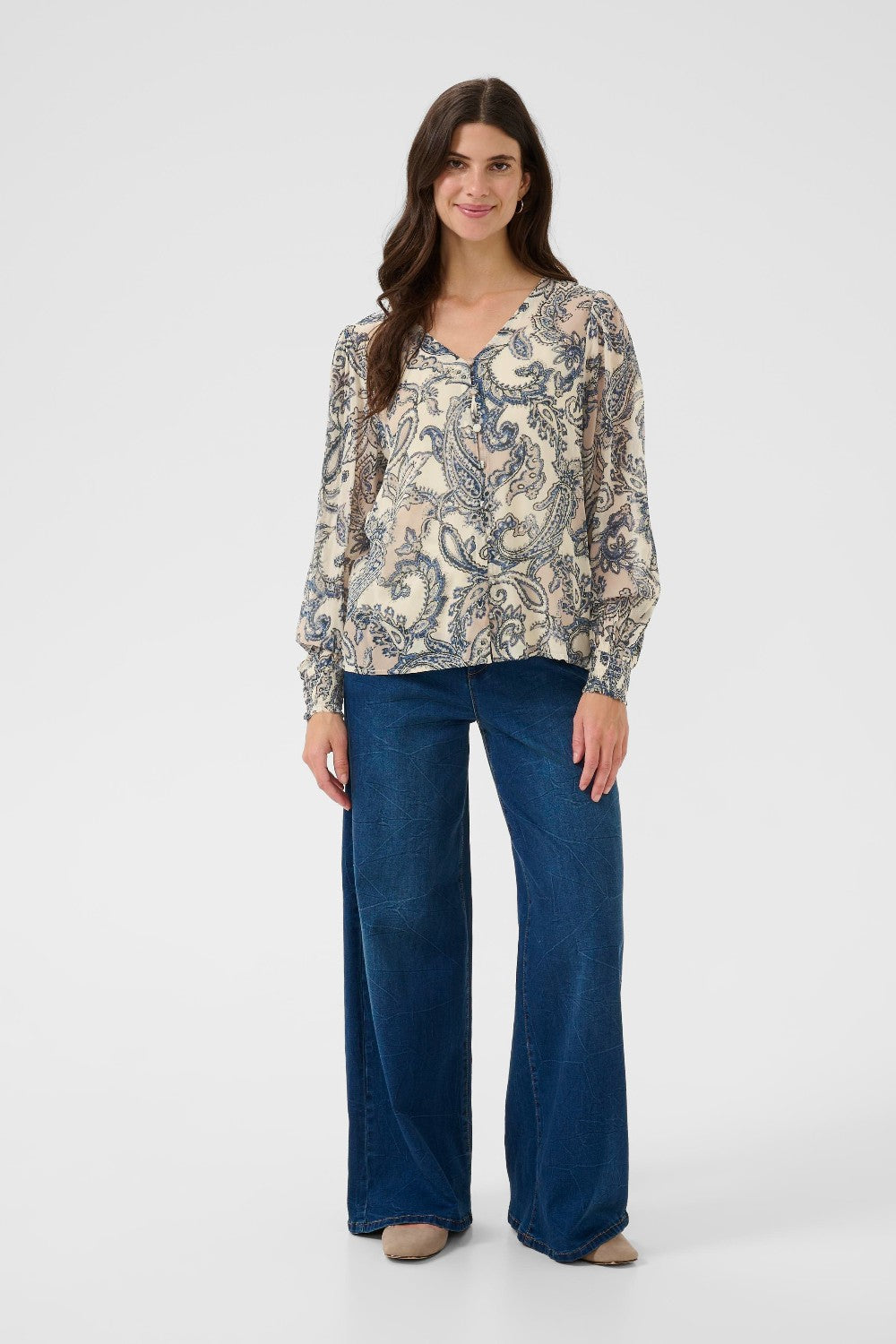 Woman wearing a patterned blouse and blue jeans on a white background
